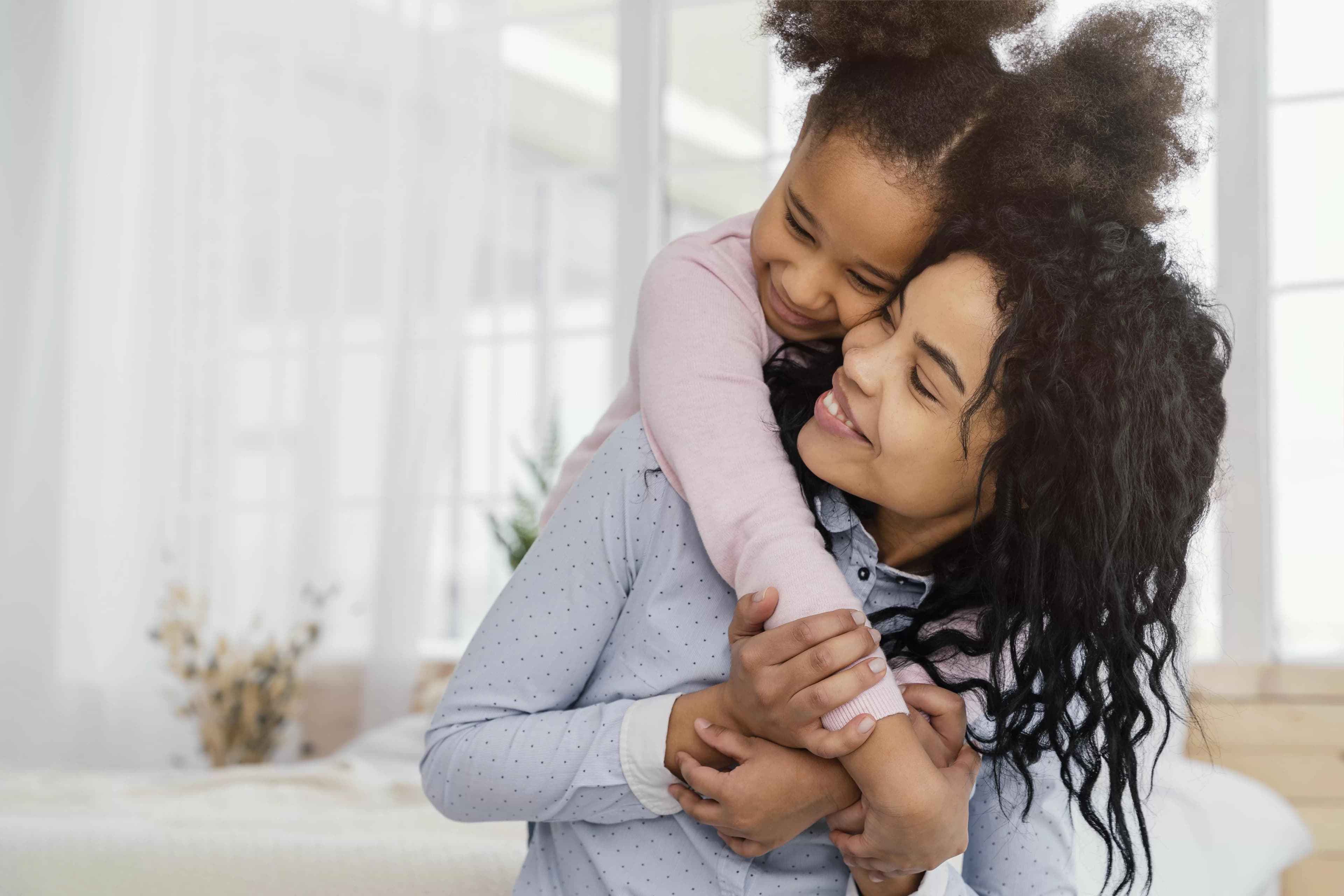 Na imagem, uma mãe e sua filha se abraçam.