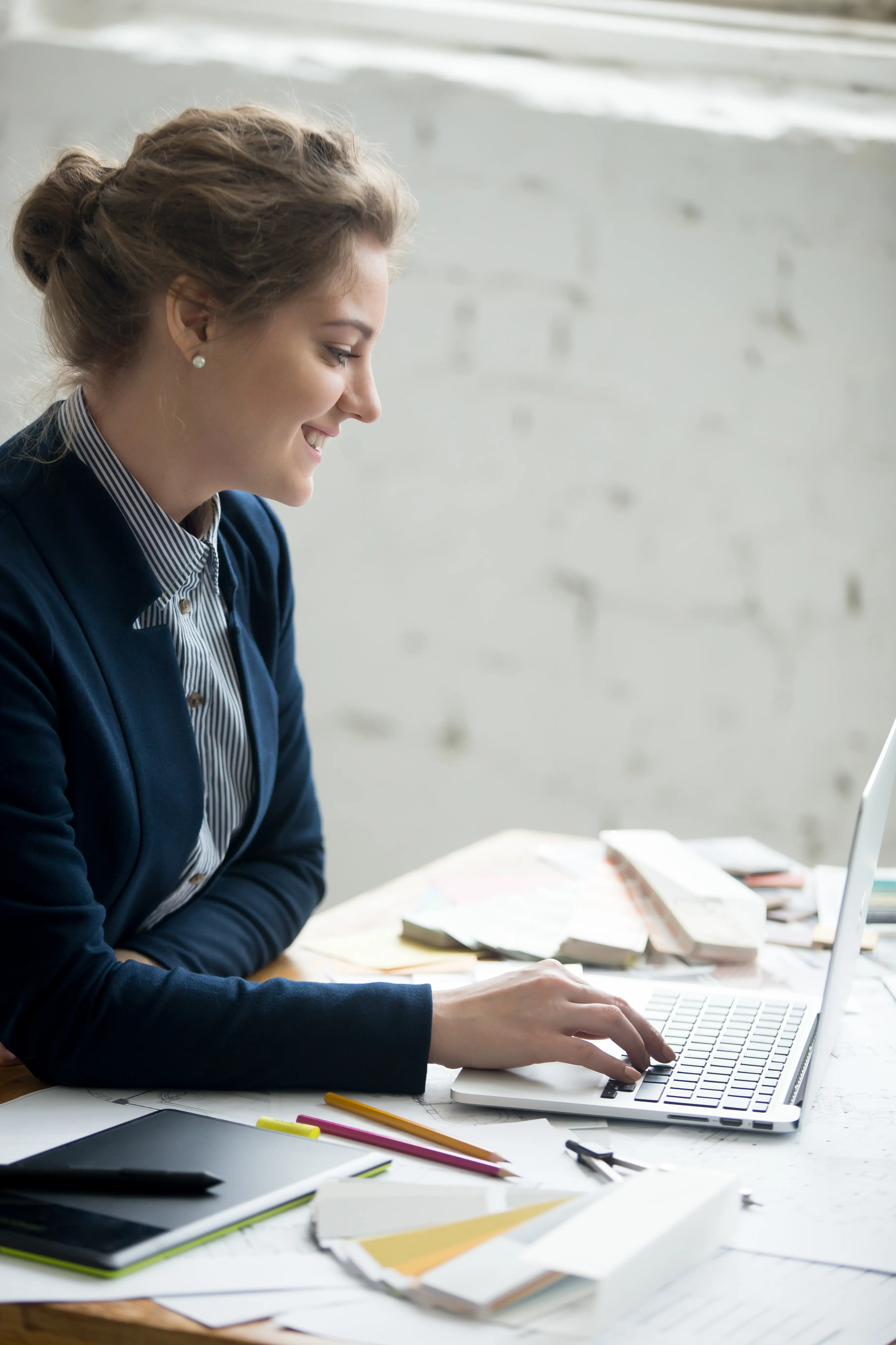 Mulher com cabelo amarrado e blazer azul está digitando em um notebook